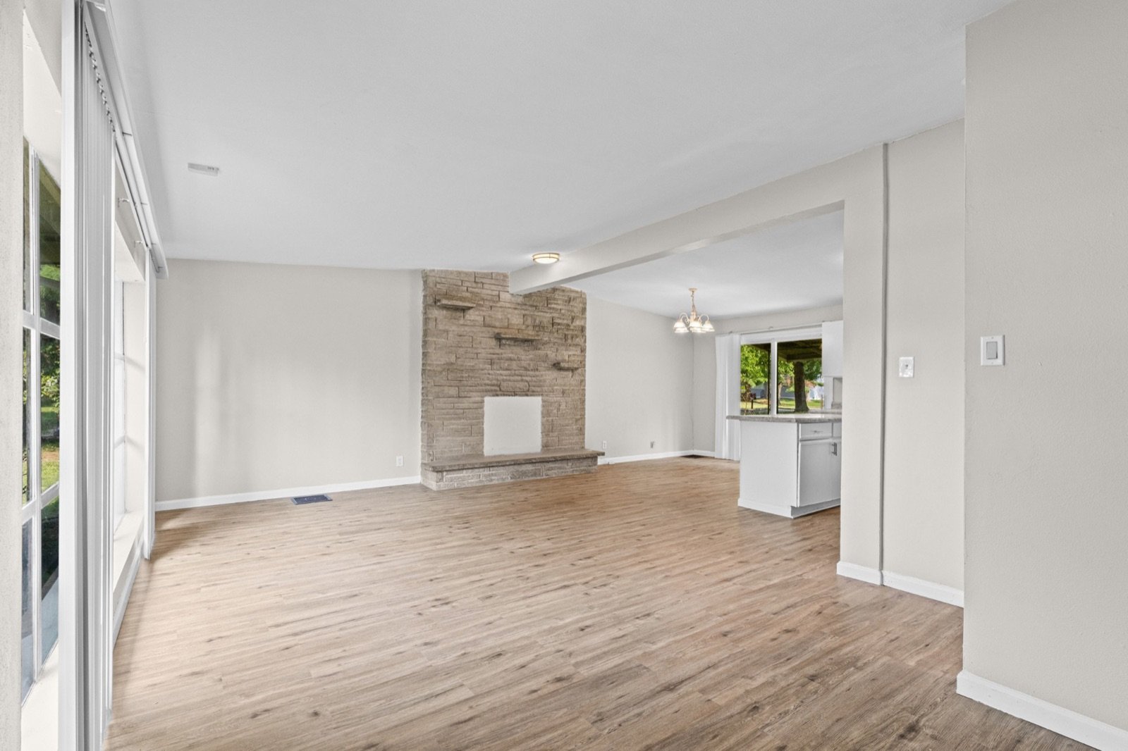 Open living room with a stone fireplace, wood-look floors and a view into the kitchen in the 2 bed, 1 bath St. Louis listing